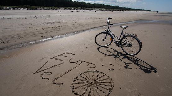 Fahrrad am Strand, im Vordergrund die Schrift "Euro Velo" im Sand