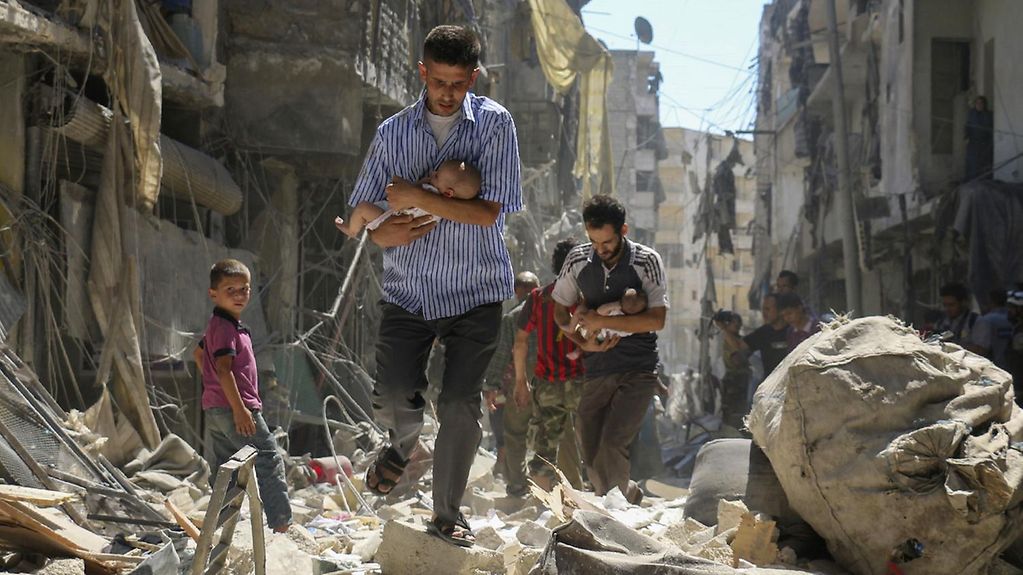Ein Mann rettet in Syrien ein kleines Kind aus Trümmern.
