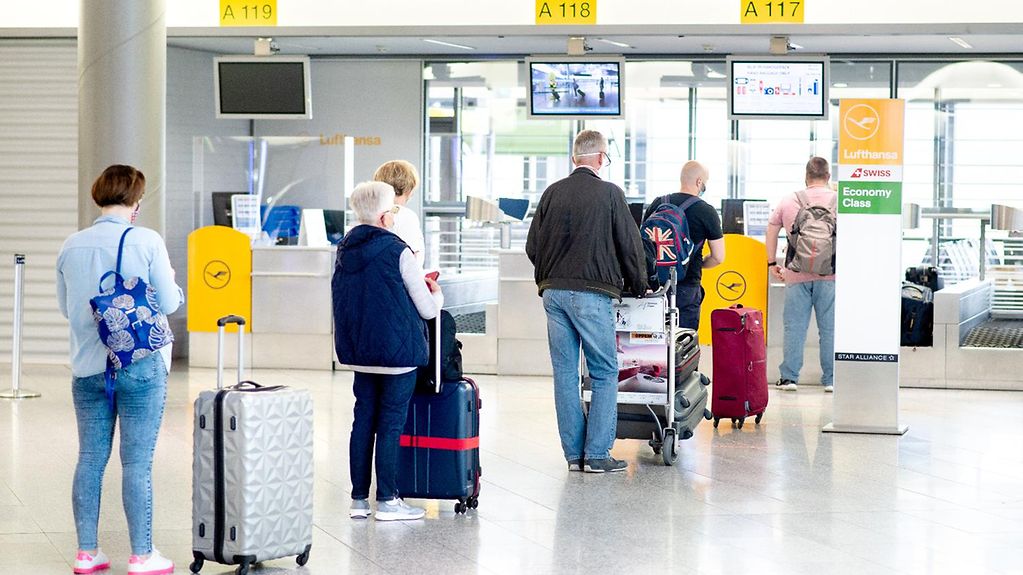Fluggäste stehen mit ihrem Gepäck vor einem Check-in-Schalter in der Abflughalle eines Flughafens.