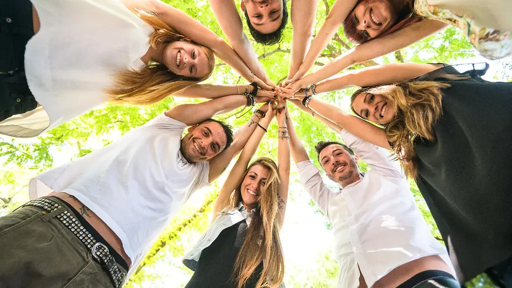 Eine Gruppe Jugendlicher in der Natur fasst sich an den Händen.