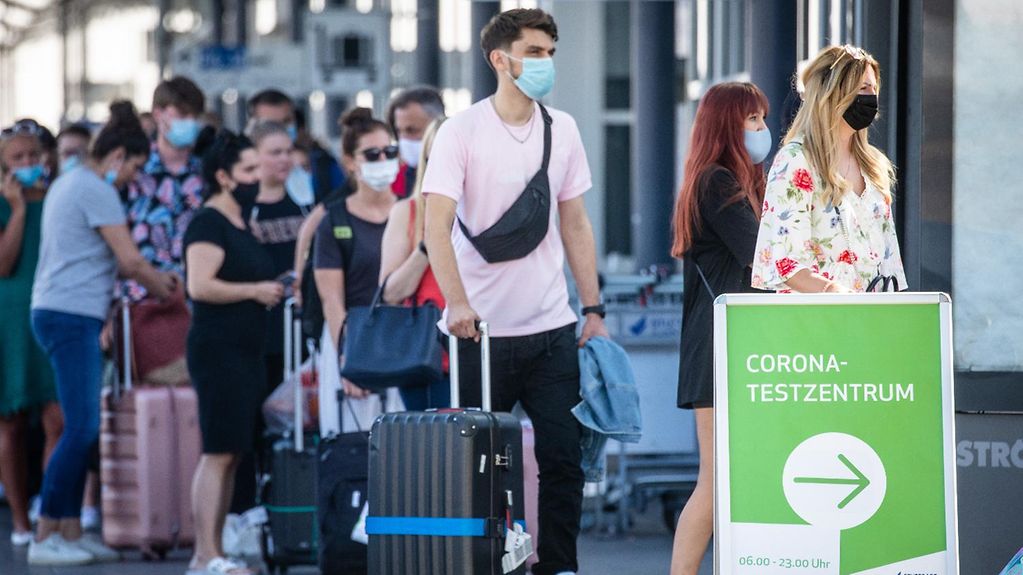 Reiserückkehrer stehen mit Mundschutz vor dem Corona-Testzentrum am Flughafen Stuttgart