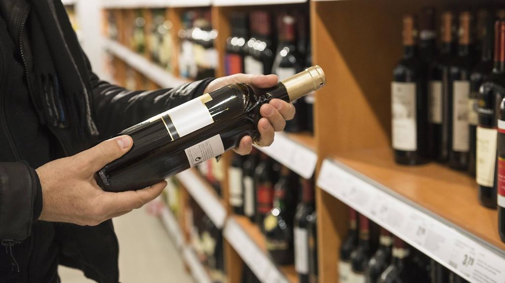 Ein Kunde betrachtet das Etikett einer Rotweinflasche an einem Weinregal.