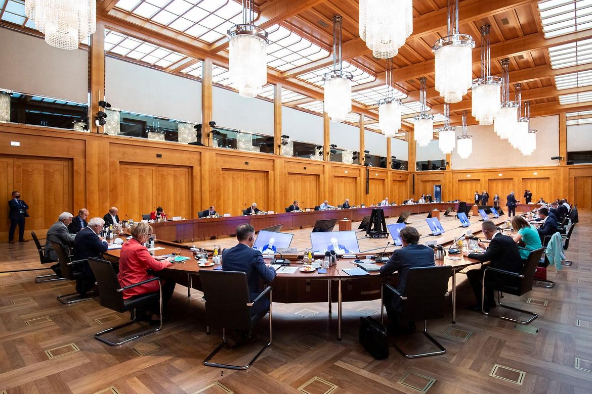 Die Außenminister sitzen an einem großen ovalen Holztisch in einem mit Holz vertäfelten und alten Kronleuchtern ausgestatteten Konferenzraum.
