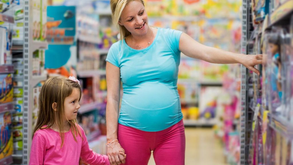 Eine schwangere Mutter geht mit ihrer Tochter durch ein Spielwarengeschäft.