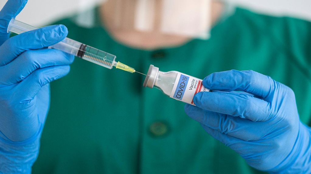 Hände in blauen medizinischen Handschuhen halten eine Spritze und eine Impfdosis.