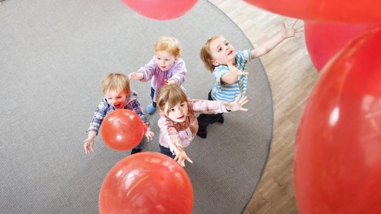 Internationaler Tag der Kinderrechte: Vier Kinder beim Spielen mit roten Luftballons im Kindergarten erhöhte Ansicht.