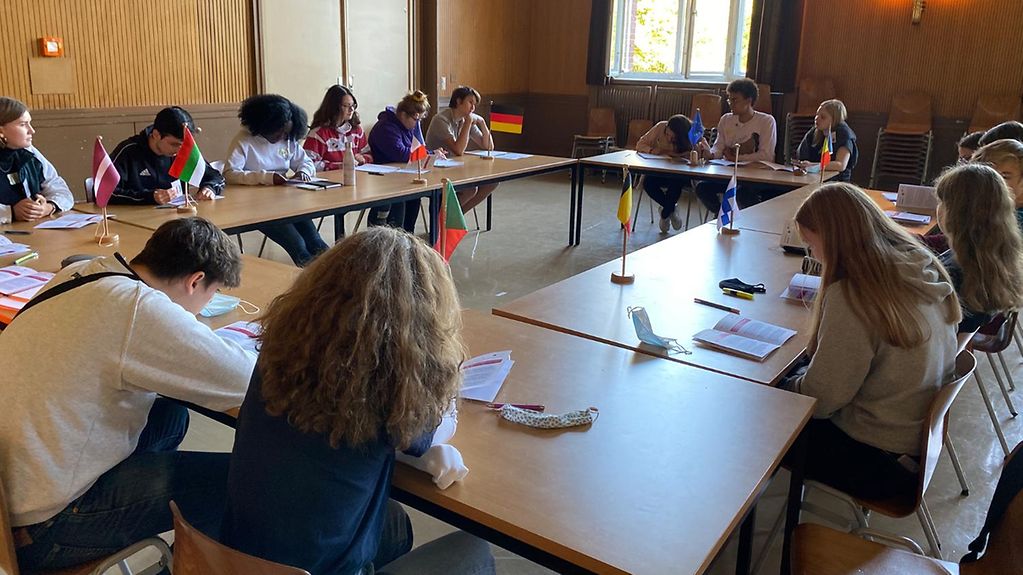 Die Schülerinnen und Schüler der Heinrich-von-Stephan-Gemeinschaftsschule in Berlin sitzen im Klassenzimmer, vor ihnen Flaggen der EU-Mitgieldsstaaten auf den Tischen.