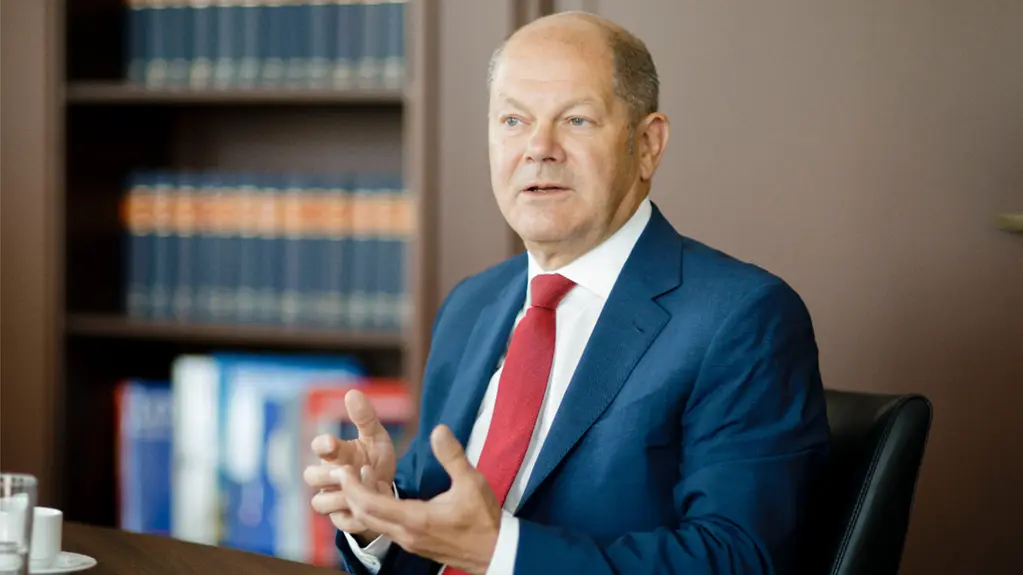 Bundesfinanzminister Olaf Scholz sitzt erklärend am Tisch