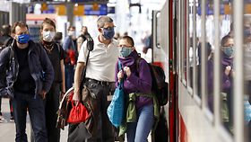 Reisende mit Masken auf dem Bahnsteig