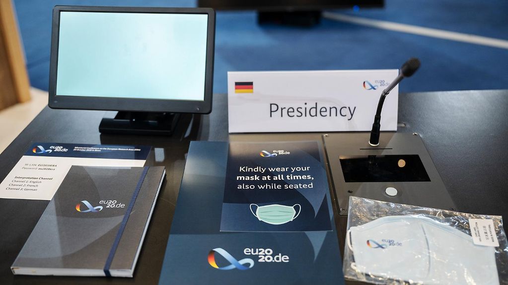 Platz der deutschen EU-Ratspräsidentschaft während einer Sitzung mit Notizblock und Mund-Nasen-Schutzmaske.