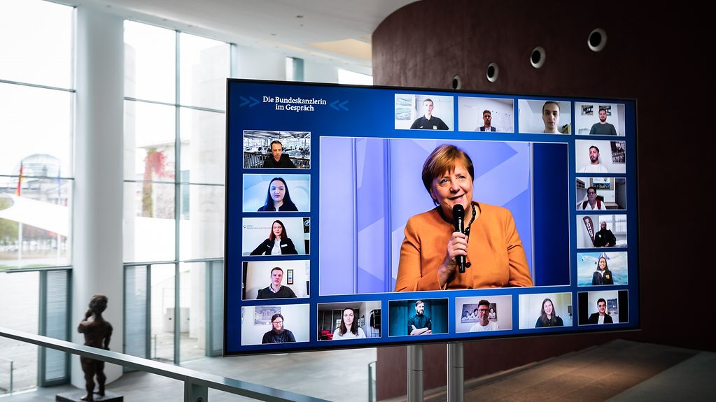 EIn Bildschirm im Kanzleramt, auf dem die Kanzlerin und die Teilnehmerinnen und Teilnehmer des digitalen Bürgerdialoges zu sehen sind.