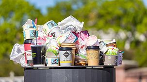 Das Foto zeigt einen mit Verpackungsmüll überfüllten öffentlichen Mülleimer.