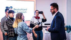 Jugendliche führen ein Interview mit dem Oberbürgermeister Rostocks, Claus Ruhe Madsen, und filmen mit Smartphones.