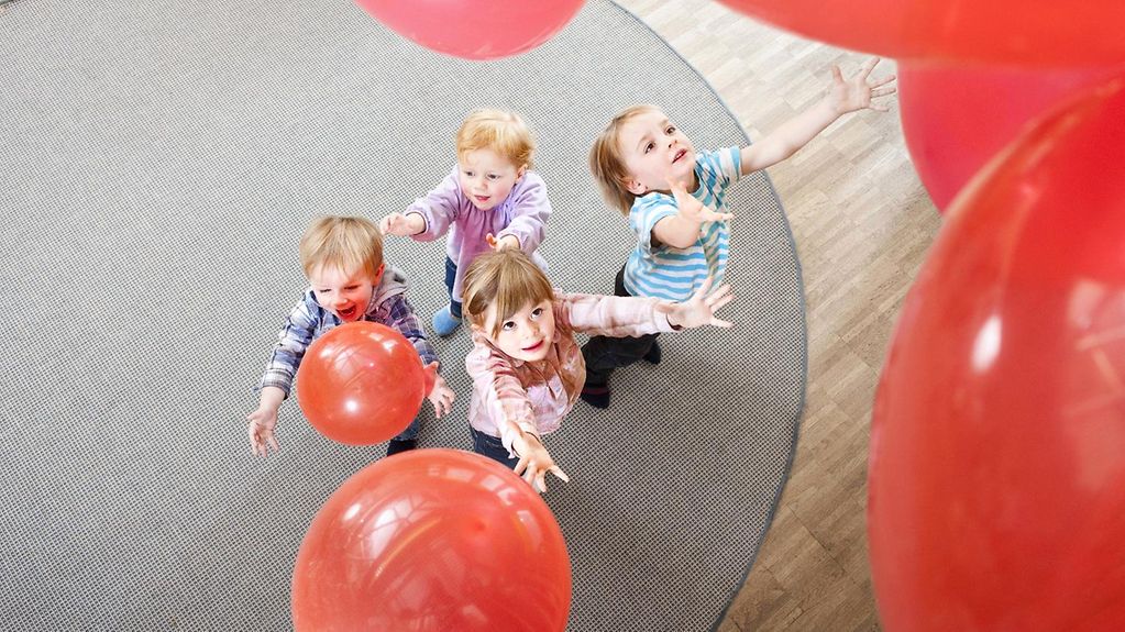 Journée internationale des droits de l’enfant : quatre enfants jouent avec des ballons rouges dans une crèche, vue plongeante