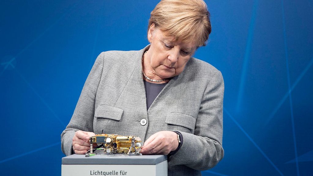 Bundeskanzlerin Merkel betrachtet ein Lichtquelle für sichere Quantenkommunikation