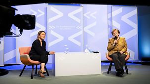 Bundeskanzlerin Angela Merkel während einer Videokonferenz neben Moderatorin Tina Gerhäusser.