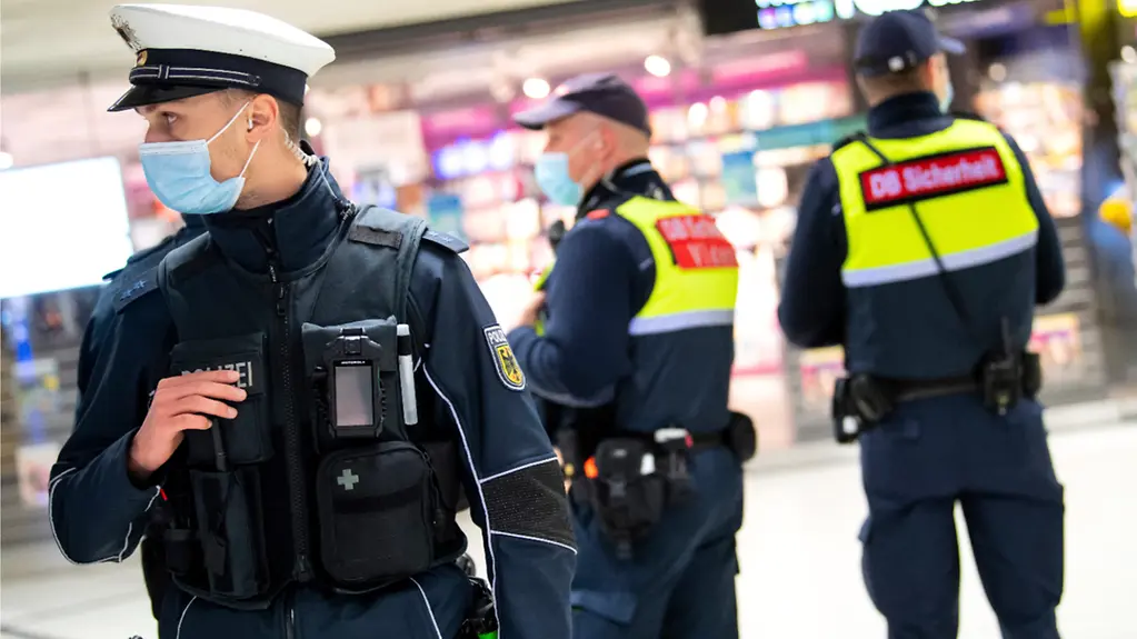 Ein Bundespolizist und zwei Mitarbeiter der Deutschen Bahn kontrollieren die Einhaltung der Maskenpflicht in einem Banhnhof.