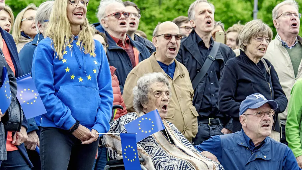 Des personnes de tous âges avec des fanions et des symboles de l’Europe chantent ensemble 