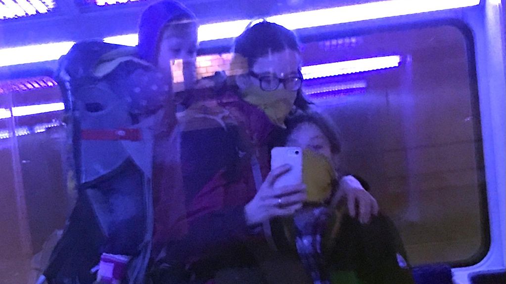 Eine Mutter mit zwei Kindern nimmt ein Selfie aus, gespiegelt in der Scheibe einer fahrenden U-Bahn.