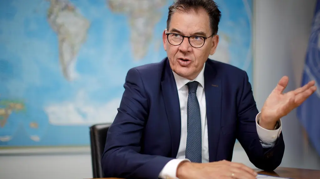 Das Bild zeigt Minister Müller, der an einem Tisch sitzt. Hinter ihm ist eine Weltkarte zu sehen.