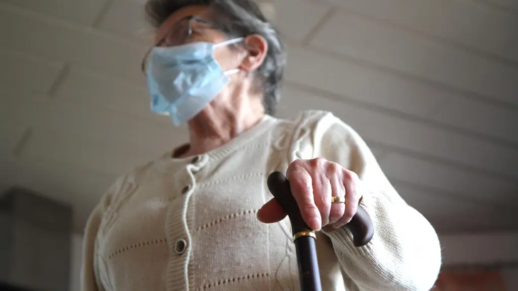 Ältere Frau mit OP-Maske und Gehstock.