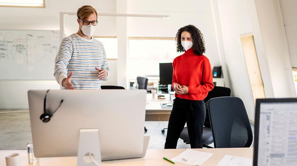 Foto zeigt zwei Mitarbeiter im Büro mit Masken. 