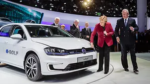 Chancellor Angela Merkel stands beside an electric Volkswagen Golf.