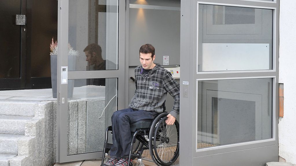 Ein Mann fährt in einem Rollstuhl aus einem für ihn installierten Aufzug.