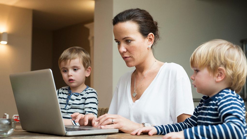 Une mère travaillant sur ordinateur avec ses deux petits garçons