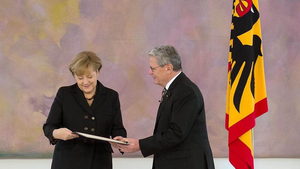 Federal President Joachim Gauck presents Chancellor Angela Merkel with her letter of appointment.