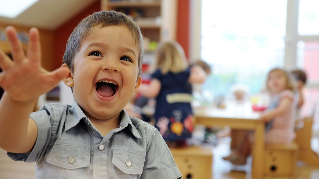A room inside a nursery, with a laughing boy in the foreground