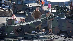 Ein Besucher steht mit einem Soldaten auf einem Panzer.
