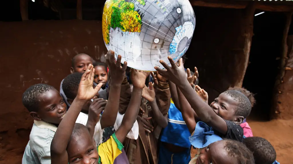 Schulkinder in Afrika spielen mit einer Weltkugel.