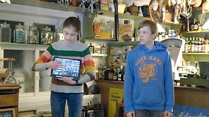 Ein Mädchen und ein Junge in einer Raum des Museums. Das Mädchen zeugt auf einem Tablet, wie man virtuell eine Führung durch das Museum machen kann.