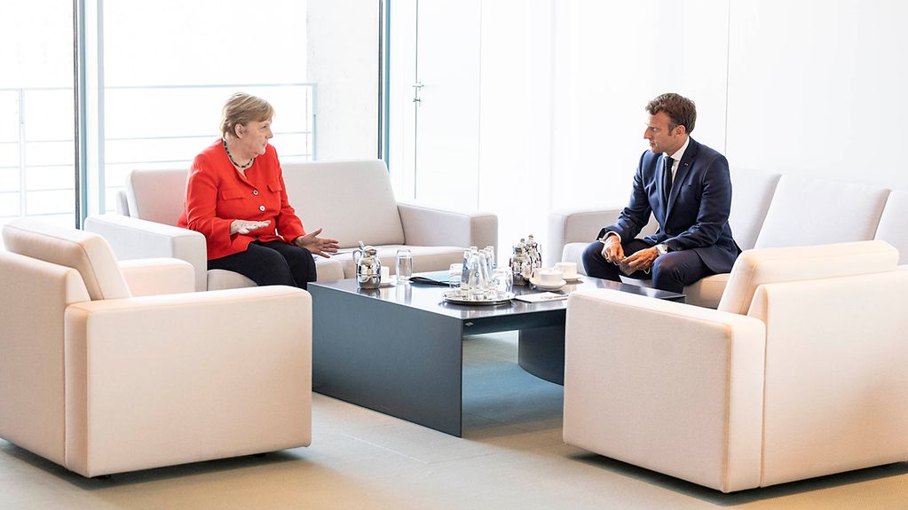 Kanzlerin Merkel und Präsident Macron sitzen nebeneinander auf zwei Sofas