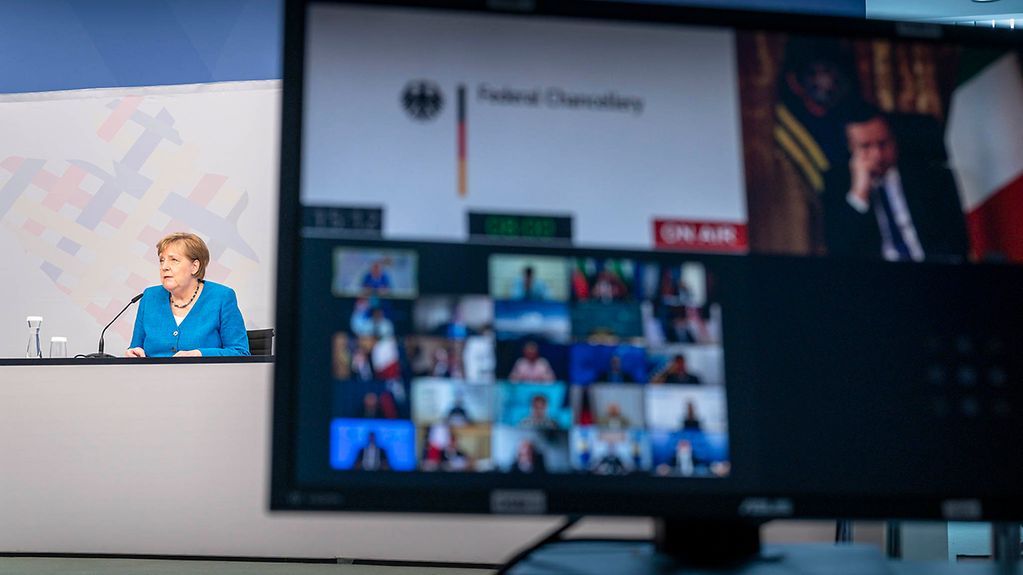 Das Bild zeigt einen Monitor mit den Teilnehmern des Westbalkangipfels. Auf der linken Seite ist Kanzlerin Merkel an einem Tisch zu sehen.