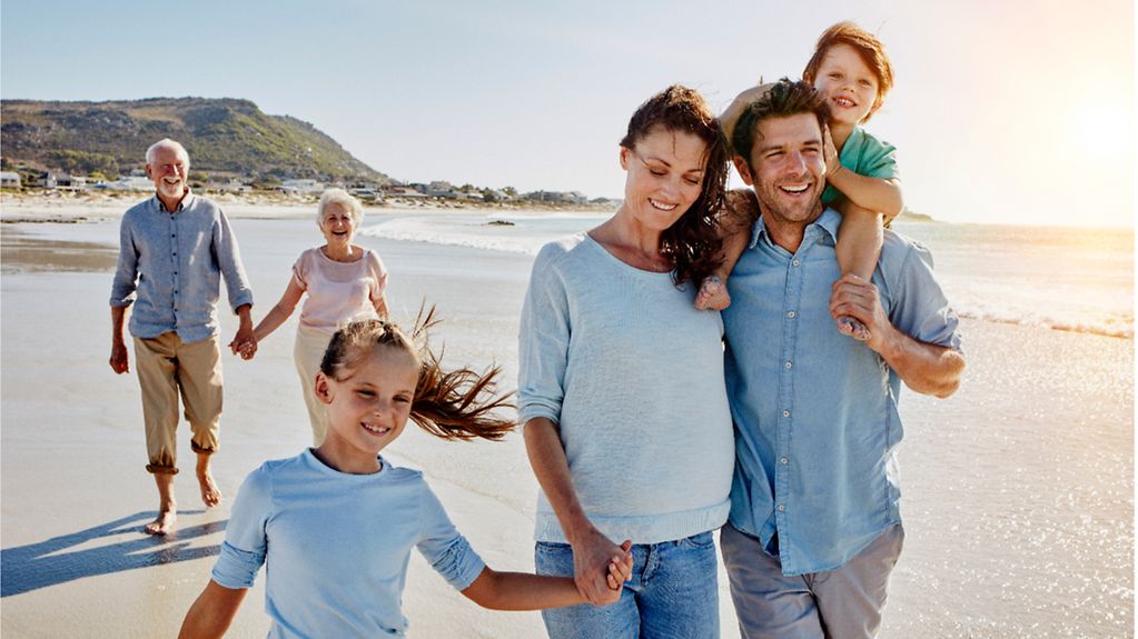 Familie am Strand: Eltern mit Kinder und Großeltern gehen am Strand spazieren.