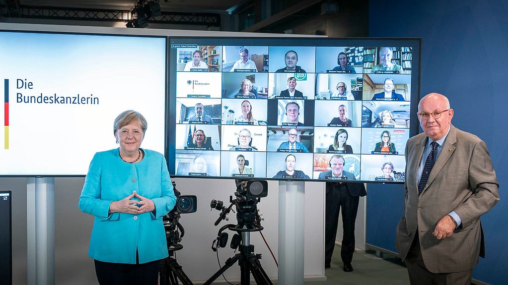 The Chairman of the Commission on the Future of Agriculture, Peter Strohschneider, and Federal Chancellor Merkel, with the members of the Commission behind them on a screen, in attendance via link.