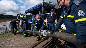 Federal Agency for Technical Relief personnel haul hoses to the banks of the Steinbach dam in Euskirchen.