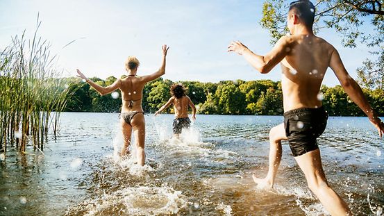 Das Bild zeigt eine Gruppe junger Menschen, die ins Wasser eines Sees rennt.