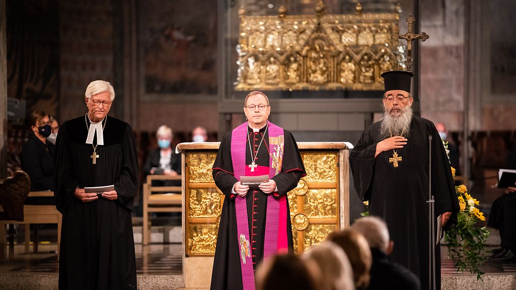 Das Bild zeigt Landesbischof Heinrich Bedford-Strohm, Bischof Georg Bätzing sowie Erzpriester Radu Constantin Miron vor dem Altar