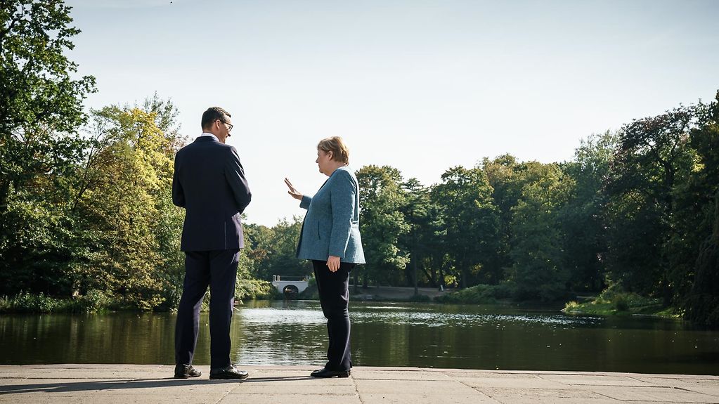 Ministerpräsident Morawiecki und Kanzlerin Merkel unterhalten sich in Warschau am Ufer eines Sees.