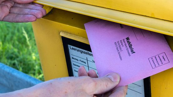 Eine Person wirft Briefwahlunterlagen in einen Briefkasten.