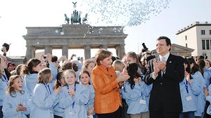 Merkel und Barroso mit Kindern vor dem Brandenburger Tor. Luftballons steigen in die Luft.