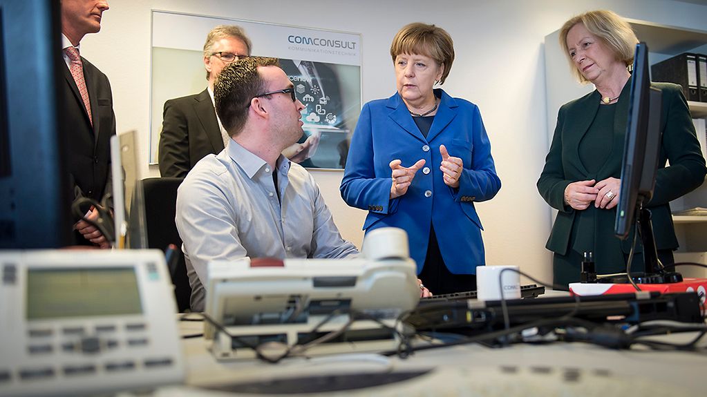 Bundeskanzlerin Angela Merkel unterhält sich mit einem Auszubildenden.