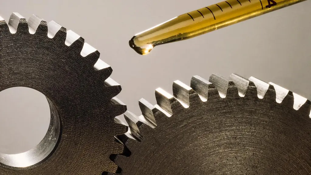 Das Bild zeigt zwei Zahnräder, darüber eine Pipette, aus der Schmierstoff tropft.