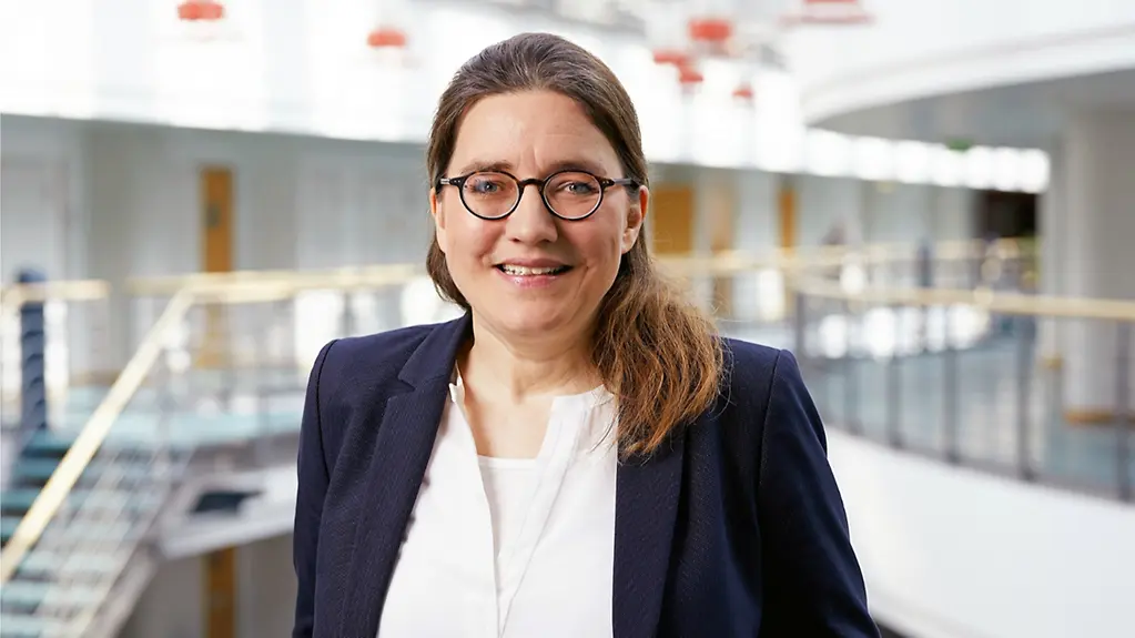 Prof.Regina Ensenauer trägt eine Brille und hat lange, dunkelbraune Haare. Sie trägt eine helle Bluse und einen dunklen Blazer.