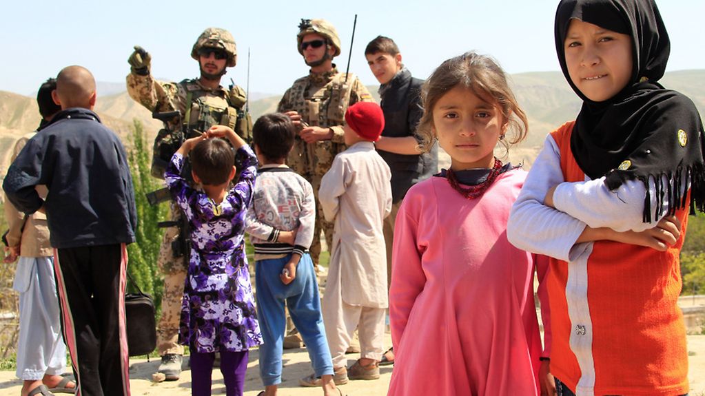 Kinder in Afghanistan, im Hintergrund sprechen Soldaten mit Menschen