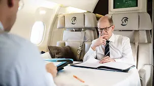 Bundeskanzler Olaf Scholz liest im Flugzeug.