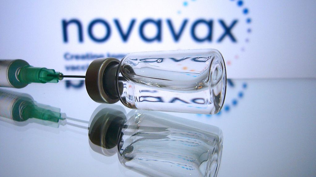 Impfdosen mit Impfstoff zur Injektion mit einer Kanuele, im Hintegrund der Schriftzug "novavax".